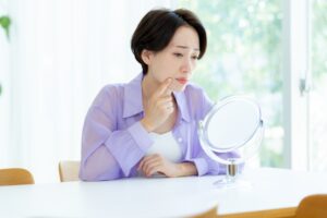 鏡を見て悩む女性｜表情筋と美容鍼の関係｜顔の印象が変わる理由とは？